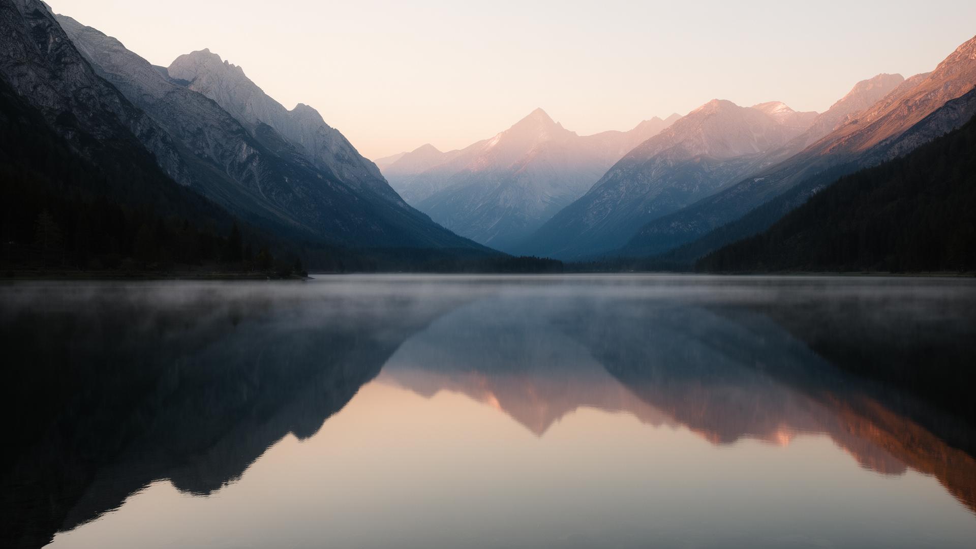 Stiller Alpensee bei Tagesanbruch mit klarer Spiegelung der umliegenden Berge